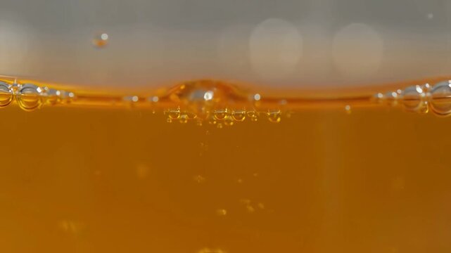 Macro close up of refreshing golden liquid with bubbles rising and popping in a glass.