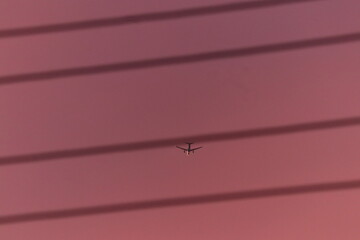 Airplane flying in pink sunset sky viewed through blurred power lines
