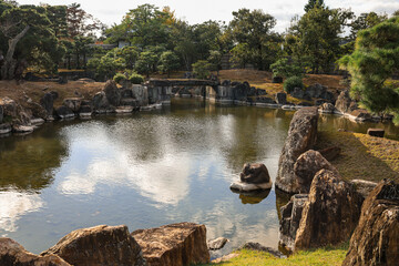 Serene Rock Garden Pond With Stones, Trees, And Reflective Water In A Tranquil Garden Scene