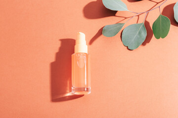 Orange cosmetic bottle and eucalyptus leaves on orange background in sunlight. Top view, flat lay, copy space