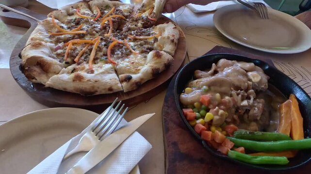 Handheld motion, taking a slice of sisig pizza which is a creative fusion of Italian and Filipino cuisine served at a restaurant