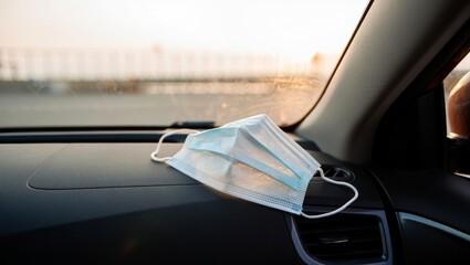 surgical mask on dashboard near passenger side with bright window light and blurred city background
