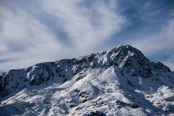 Snow-covered mountain ridge under dramatic cloudy sky. Winter alpine landscape with rugged peaks and natural textures.