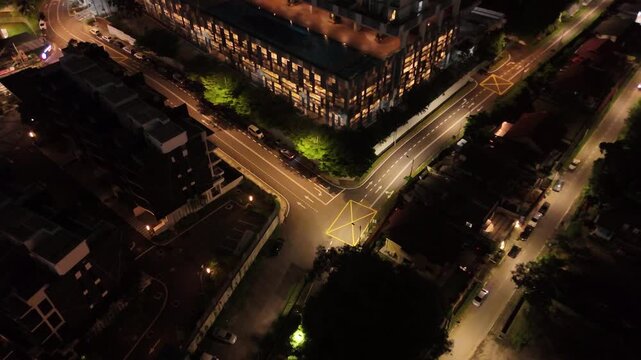Aerial b roll of a city intersection at night showing streets buildings and moving traffic illuminated by streetlights creating a dynamic urban atmosphere from above
