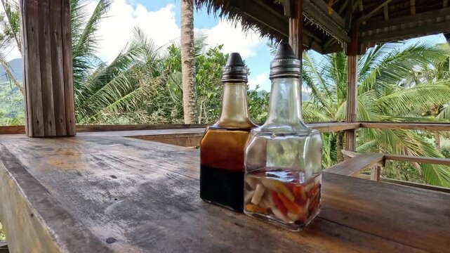 Pan right from bottles of traditional Filipino condiments on a rustic wooden table with the view of the mountains in the background that depicts a peaceful rural life in the Philippines