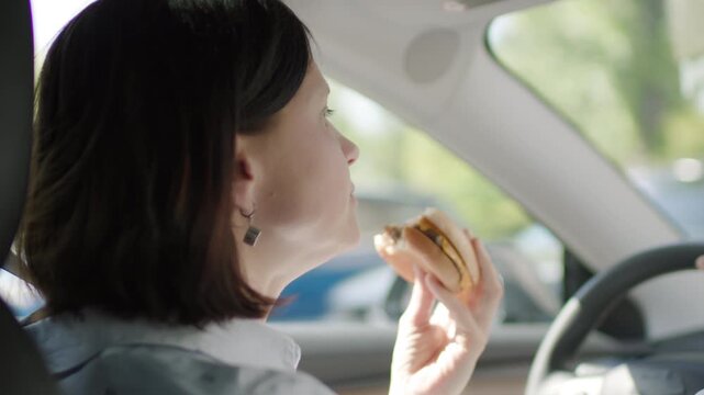 Woman eating a burger behind the wheel, showing distracted driving and road safety risk.
