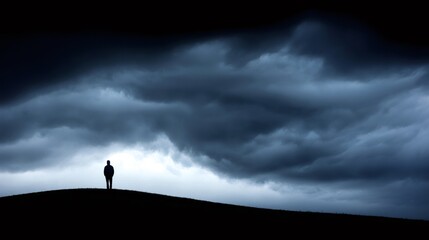 Fototapeta premium Man standing alone on a dark hill with a foreboding sky, representing depression, solitude, and difficult times