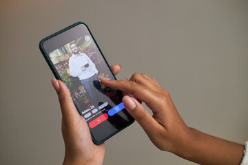 Young adult Black woman using smartphone dating app, swiping on profile of young adult Caucasian man, hand holding phone with dating interface visible on screen