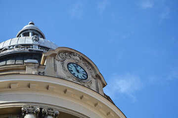 An elegant architectural dome featuring a classic analog clock face and ornate stone carvings against a bright blue sky © nahhan