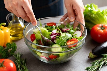 Fresh vegetable salad preparation in glass bowl with hands and natural ingredients
