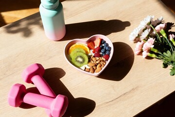 Healthy fitness lifestyle flat lay with dumbbells fruit bowl and sunlight
