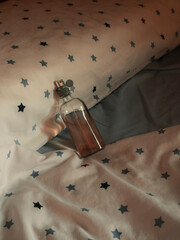 Glass bottle of perfume resting on bed with white sheets. Mockup template fragrance.