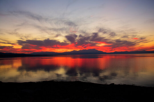 Dramatic sunset over a calm lake with mountain silhouettes - Powered by Adobe