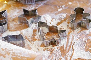 Baking gingerbread cookie cutters, wooden rolling pin, and flour are messily spread on rustic kitchen table. Process of cooking festive traditional Christmas sweets, bakery