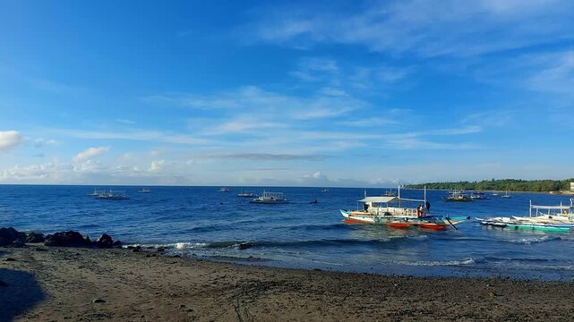 A sunny day at the beach with outrigger boats anchored and bobbing with the waves in a hypnotic rhythm under a clear blue sky in the Malatapay wharf. Dauin, Negros Island, Philippines