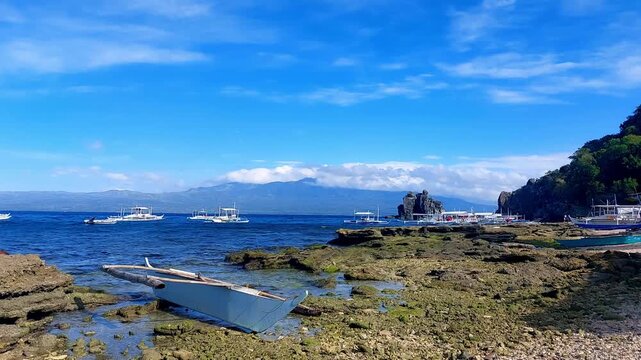 Calm soothing summer paradise scene of outrigger boat moored in the rocky beach and in the horizon of Apo Island, Philippines