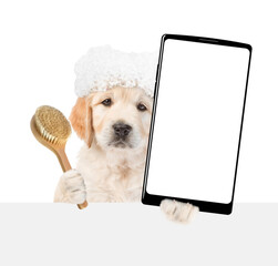 Golden retriever puppy with soap foam on it head holds shower brush and big smartphone with white blank screen in it paw above blank white banner. isolated on white background