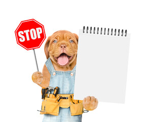 Happy mastiff puppy wearing denim overalls with tool belt shows stop sign and blank notepad. Isolated on white background