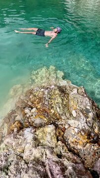 Candid authentic moment of a man floating in turquoise waters surrounded by rocky cliffs and forest in JABA sulfur lagoon in Tanjay, Negros Oriental, Philippines