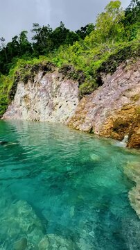 Overhead view of a man swimming in turquoise water beside a rocky cliff with surrounding lush greenery, JABA sulfur lagoon in Tanjay Negros Oriental Philippines