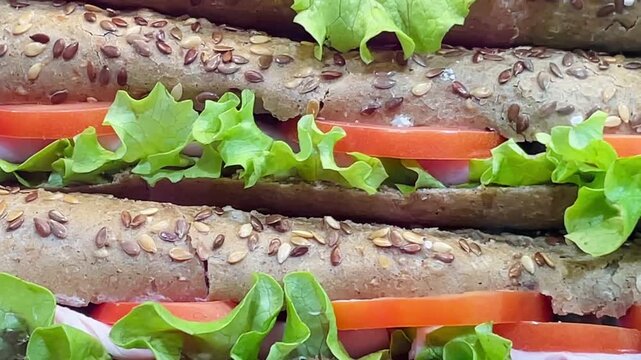 stacked multigrain seeded bread sandwich layers with crisp lettuce and ripe tomato slices, closeup showcasing sesame and flax seeds, vibrant colors and crunchy texture Video taken on mobile devicr.