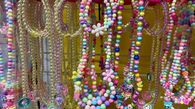 Multicolor children's necklaces and bead bracelets on a shop display. Bright jewelry with plastic flowers and figures, concept of kids fashion, gifts, and accessories for girls.