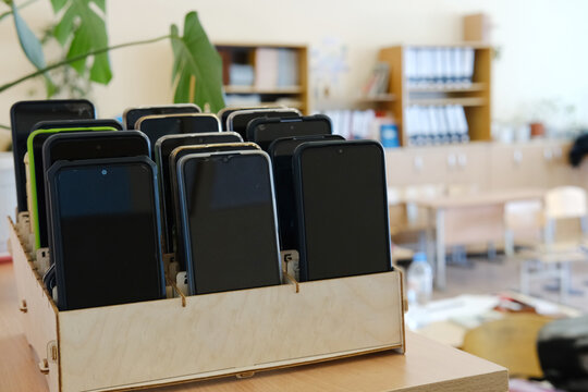 Schoolchildren's mobile phones stored in a wooden box on a classroom shelf, emphasizing the ban on devices during school hours and promoting focus on learning and education