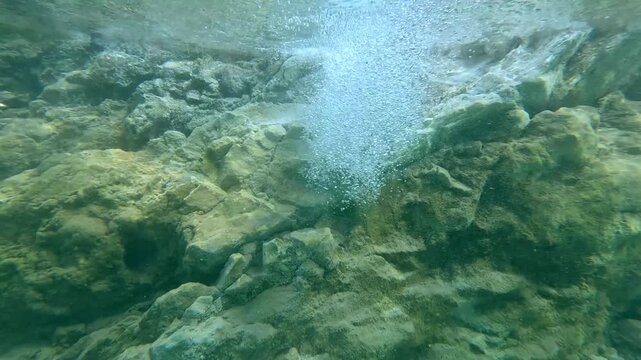 Underwater dolly up to breaking the water surface, revealing a flowing natural spring among volcanic rocks that creates an otherworldly scene in JABA sulfur lagoon in Amlan, Negros Oriental, Philippin