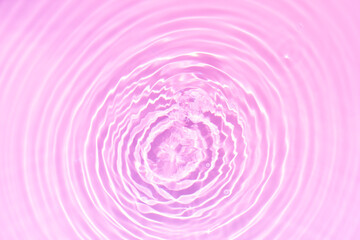 Pink water bubbles on the surface ripples. Defocus blurred transparent pink colored clear calm water surface texture with splash and bubbles. Water waves with shining pattern texture background