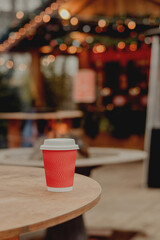 Red Takeaway Coffee Cup on Wooden Table in Cozy Outdoor Cafe