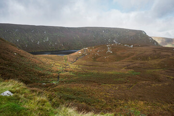 Remote Wicklow Mountains landscape at Lough Bray, corrie lake, autumn heather, mossy slopes, dramatic sky.