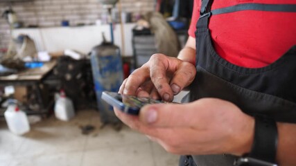 Skilled mechanic interacts with smartphone, showcasing hands covered in grease, immersed in automotive work, highlighting the connection between technology and traditional car repair methods