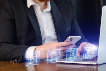 Man using phone and laptop for work tasks in office setting during daytime hours