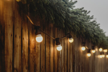 Warm String Lights on Wooden Fence with Evergreen Decor