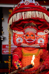 Fototapeta premium Kannur, Kerala / India – December 12, 2025: A Theyyam performer dressed in traditional red ritual costume holds a flaming torch during a Theyyam ritual performance at a temple in Kannur district