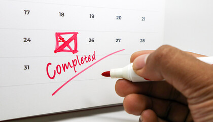 Achieving Milestones A hand marking Completed on a calendar with a red pen, symbolizing successful task completion and effective time management for personal and professional goals