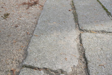 Obraz premium A gray sidewalk with a visible crack in the middle. The crack is about the size of a person's foot and runs from the left side of the sidewalk to the right. The sidewalk is made of stone
