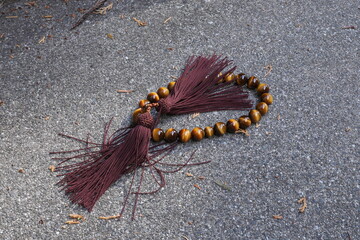 A brown and gold bracelet with a tassel hanging from it. The tassel is frayed and the bracelet is laying on the ground