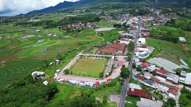 Aerial drone footage of an agricultural area in Indonesia, with many small plots of different vegetables in in the slope of Ungaran volcano and a city on the side