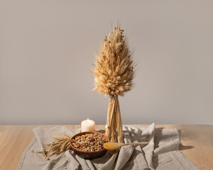 Aesthetic Ukrainian Christmas traditional background. Wooden table with national handmade decor and food. Dodukh and kutia on plate, linen tablecloth, empty neutral beige wall background