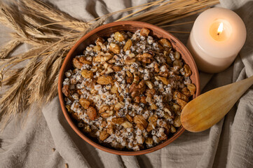 Traditional Christmas holiday food in Ukraine, kutia. Plate with wheat cereal, raisins, poppy seeds and nuts, candle light on neutral beige linen tablecloth