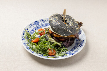 Charcoal bagel burger with fresh salad on plate