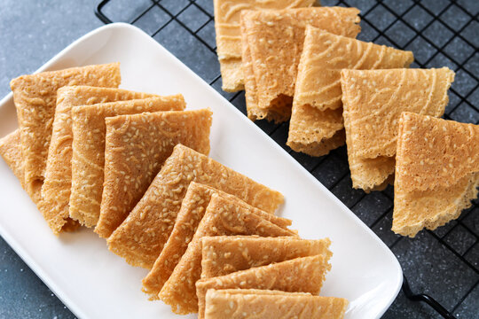 Crispy, golden-brown Kue Semprong or Love Letter cookies, a thin, folded Southeast Asian snack. Arranged on a white plate and a cooling rack, highlighting their delicate texture.