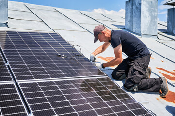 Worker building solar panel system on metal rooftop of house. Man engineer installing photovoltaic solar module outdoors. Alternative, green and renewable energy generation concept.