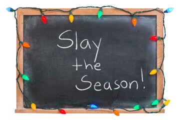 Sleigh slay the season handwritten in white chalk on a black chalkboard decorated with festive colorful holiday lights