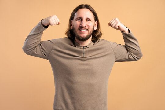 Confident man flexing biceps, showing strength and feeling powerful on beige background