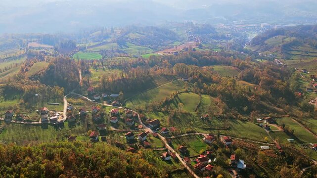 Aerial drone view of a traditional Bosnian rural landscape with scattered homes, winding roads, farmland, and forested hills