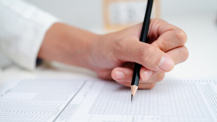Close up of hand filling answer sheet with pencil, multiple choice test form, exam assessment, survey evaluation and education or research concept.