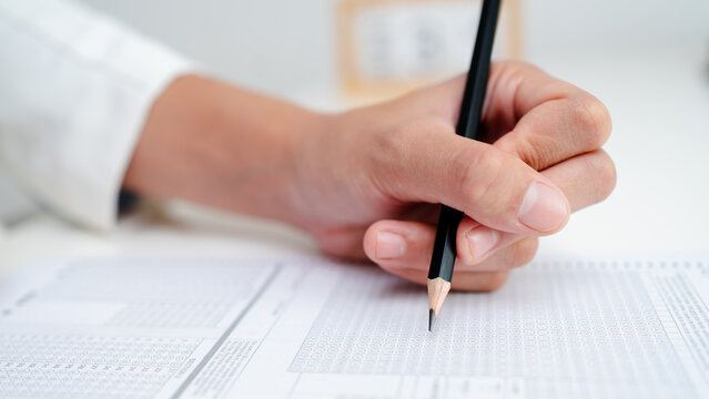 Close up of hand filling answer sheet with pencil, multiple choice test form, exam assessment, survey evaluation and education or research concept.