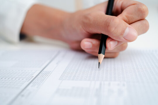 Close up of hand filling answer sheet with pencil, multiple choice test form, exam assessment, survey evaluation and education or research concept.